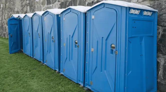 Row of blue portable toilets lined up on grass against a stone wall for event sanitation in Long Beach, CA