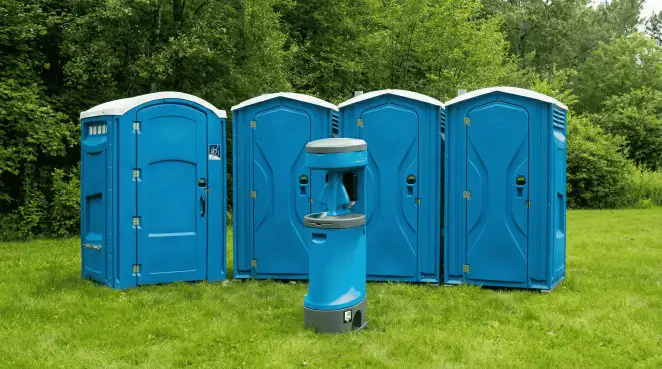 Four blue portable toilets and a matching hand washing station on grass near trees, a common sight at local outdoor events in Long Beach, CA